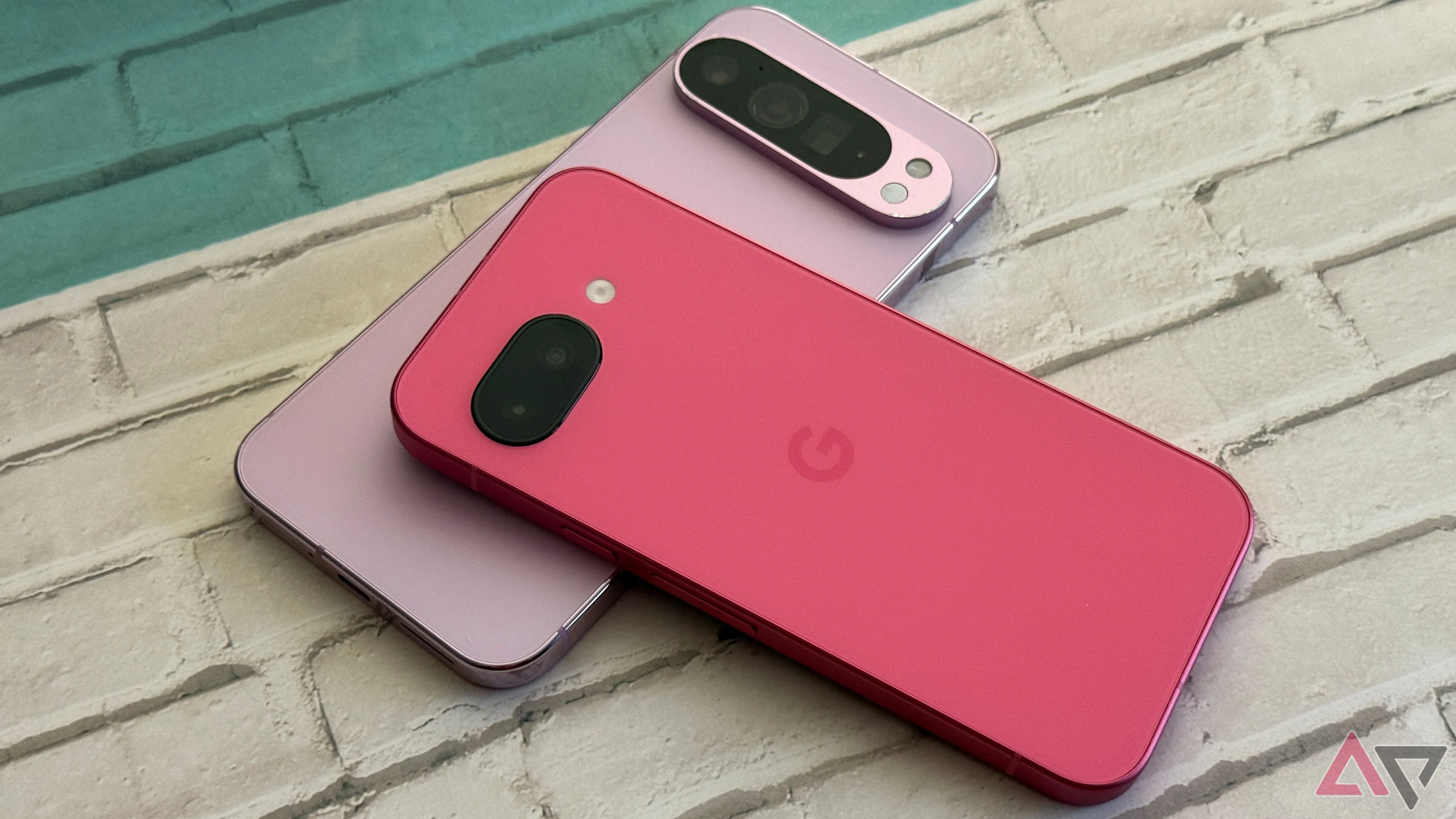 Điện thoại Google Pixel 9a màu đen nằm trên chiếc Google Pixel 9 Pro XL màu xanh lá cây, thể hiện kích thước và thiết kế của hai thiết bị.