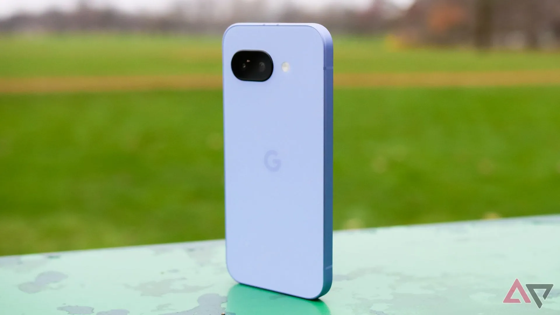 Điện thoại Google Pixel 9a màu tím đặt thẳng đứng ở công viên.