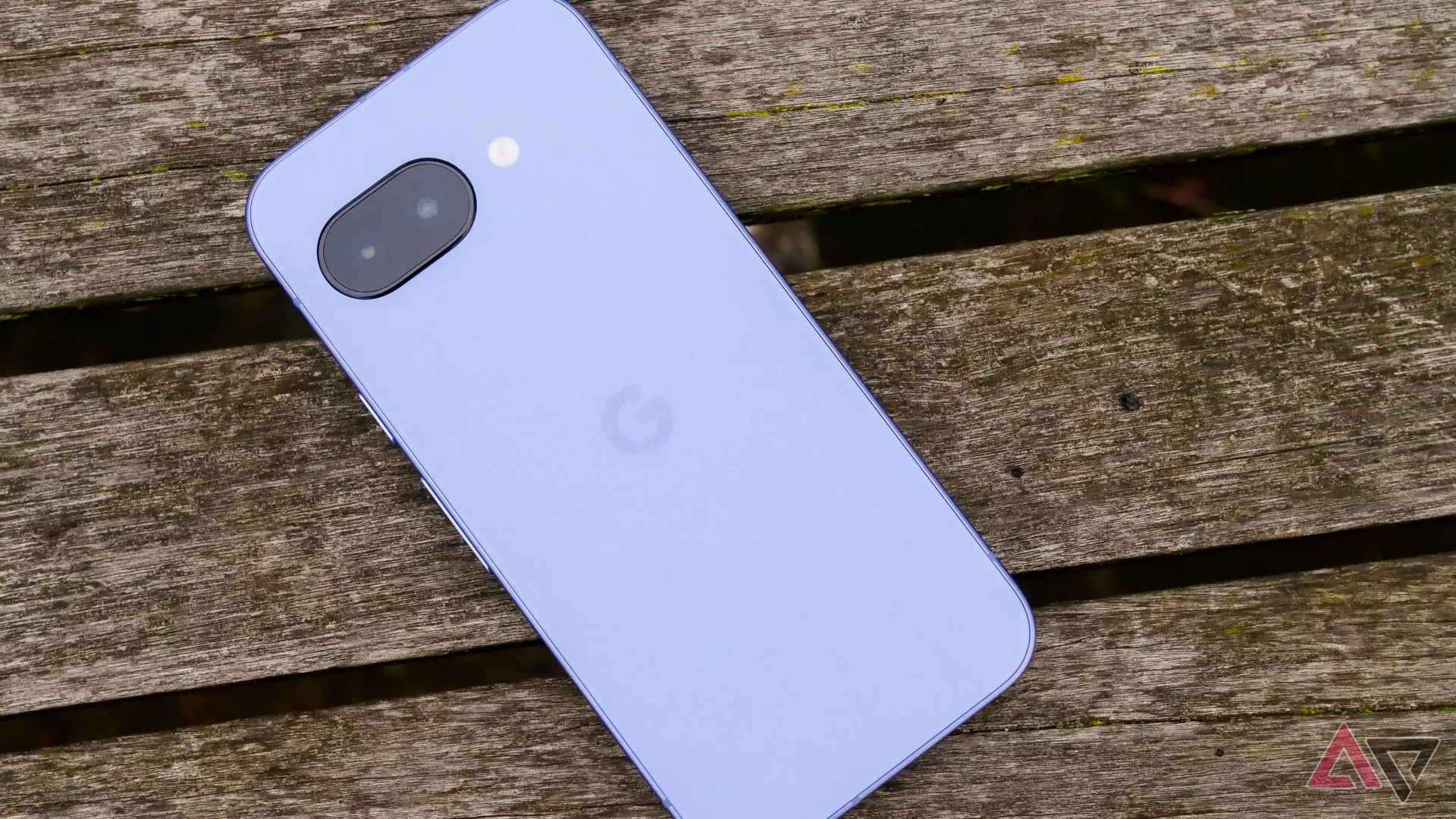 Google Pixel 9a mặt lưng tím đặt trên ghế gỗ trong công viên.