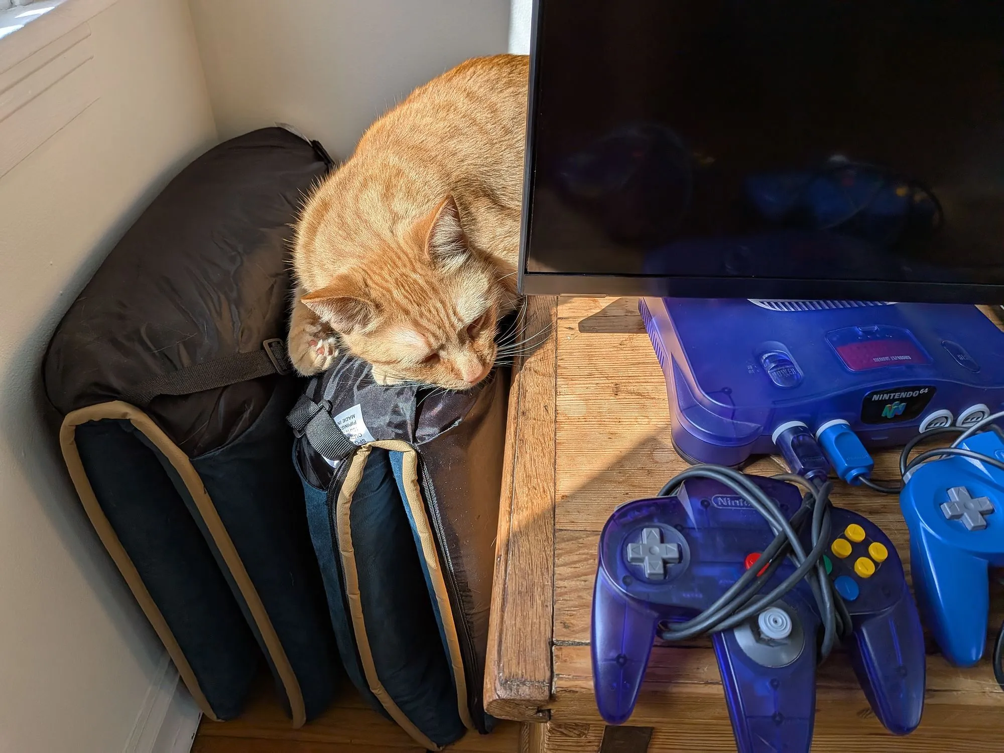Một chú mèo màu cam đang rình mò một chiếc máy chơi game Nintendo 64, màu sắc sống động.