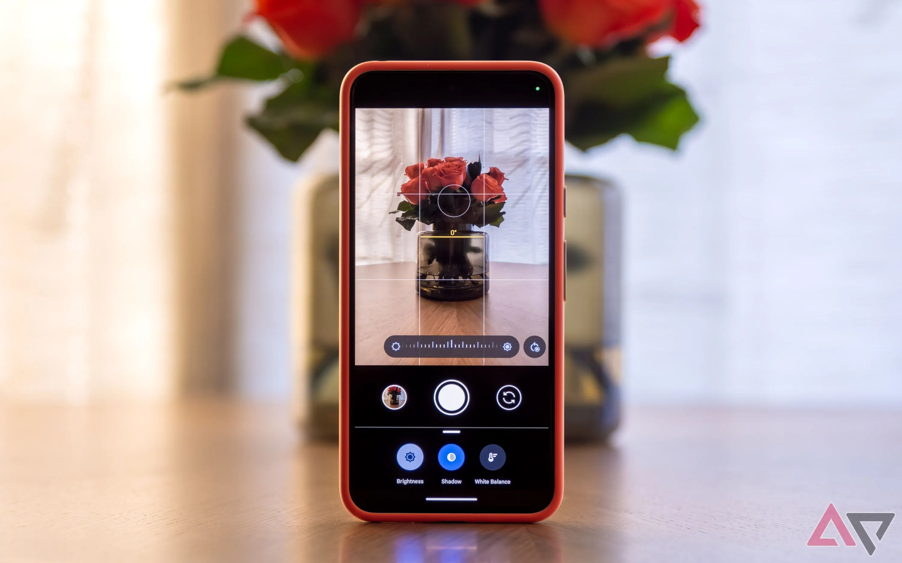 Ứng dụng Camera trên điện thoại Pixel đặt thẳng đứng trên bàn cạnh bình hoa, hiển thị các đường lưới và gợi ý khung hình.