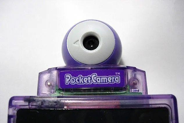 Thiết bị Game Boy Camera gắn trên Game Boy màu tím, cho phép chụp ảnh và in ngay lập tức.