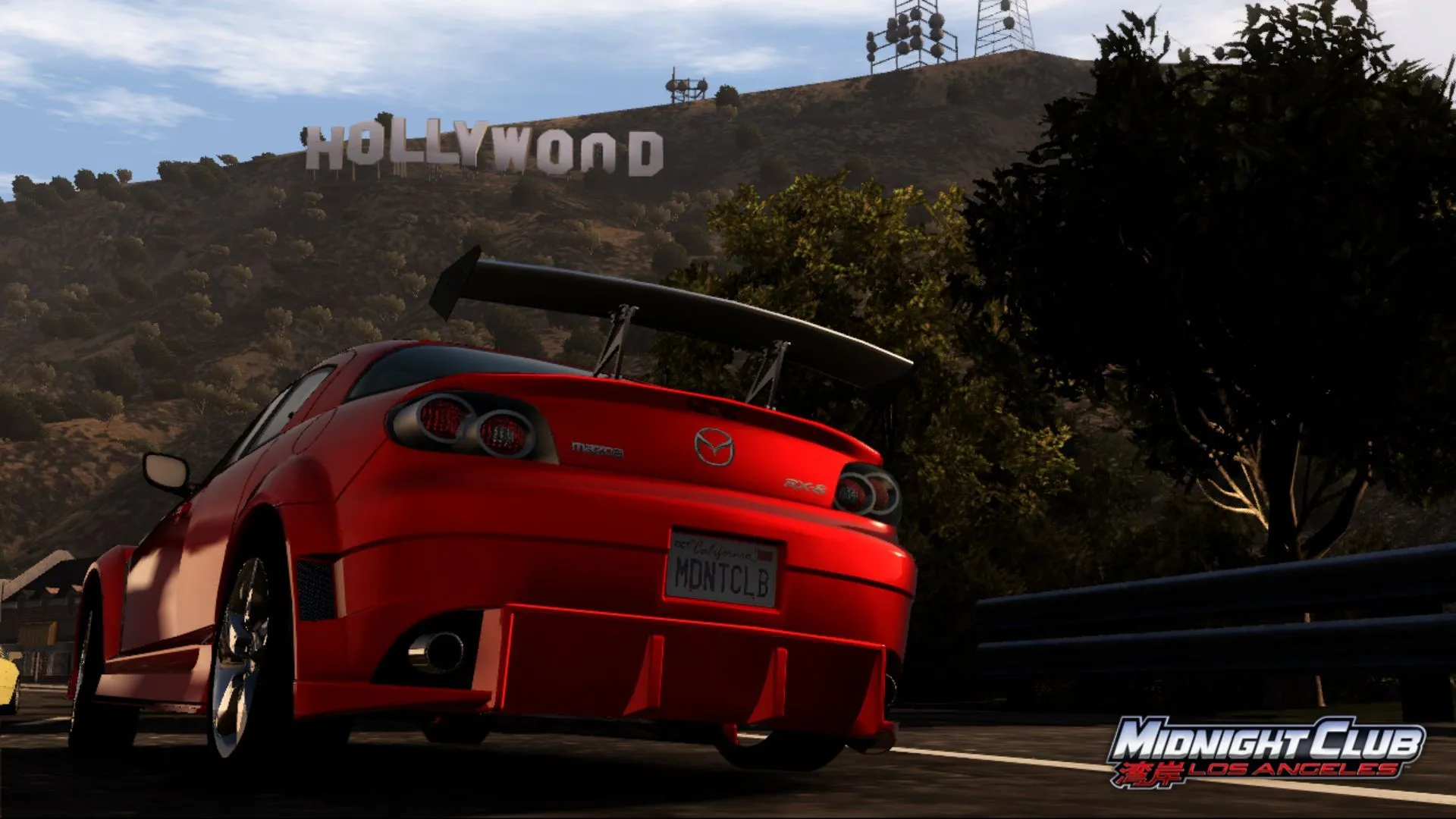 Ảnh chụp màn hình game Midnight Club: Los Angeles với xe Mazda màu cam trên đường phố, phía sau là biểu tượng Hollywood