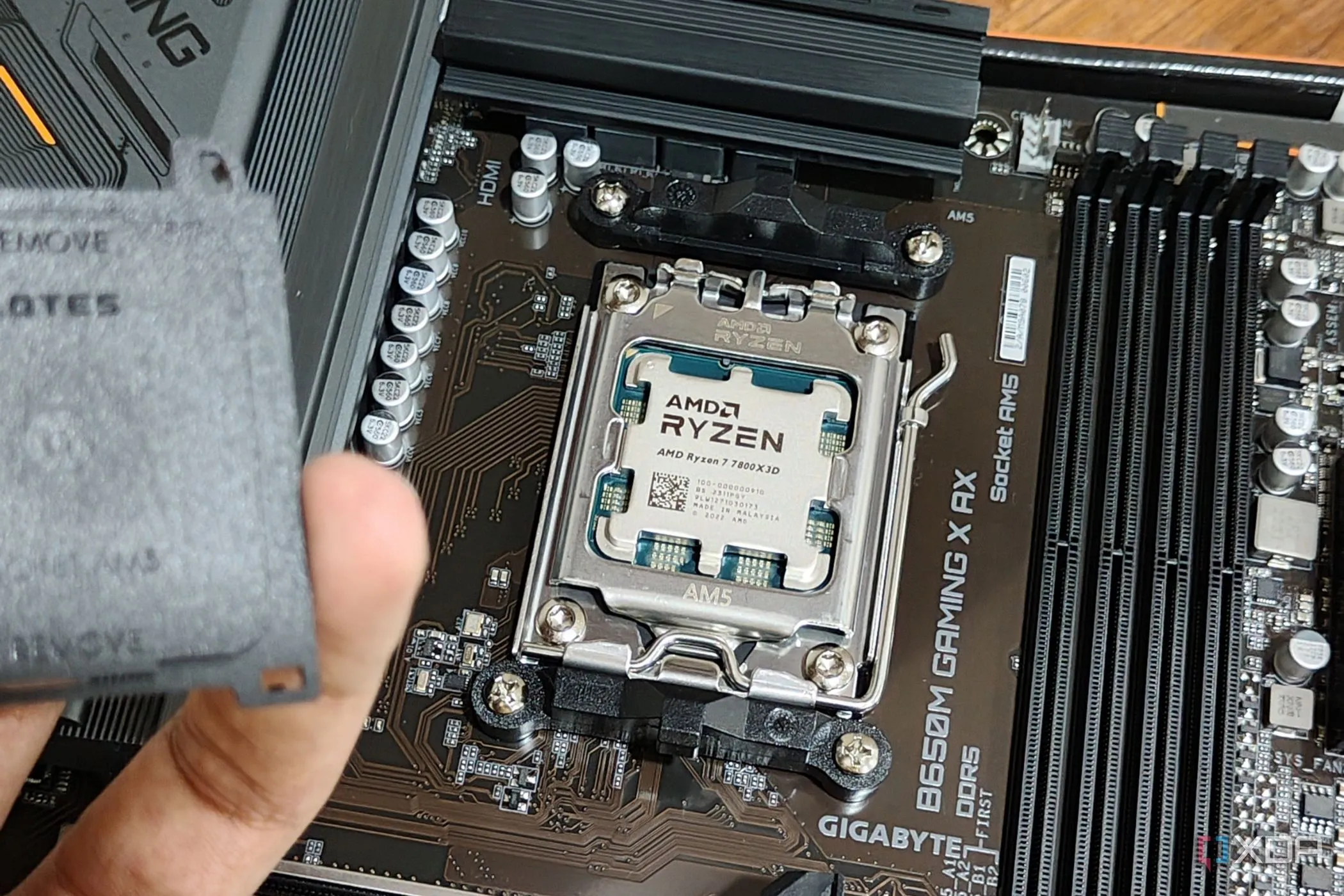 Bo mạch chủ với CPU AMD Ryzen 7 7800X3D được lắp đặt, một người đang cầm nắp socket ở tiền cảnh