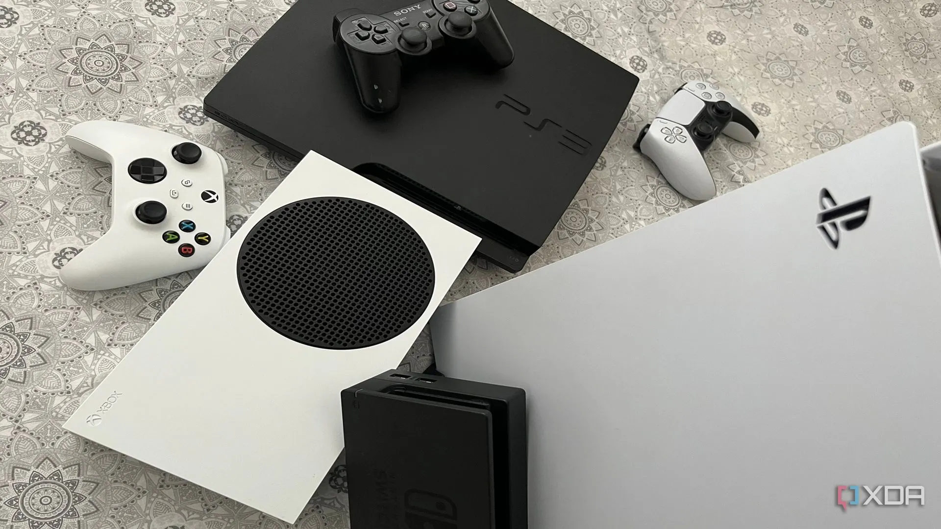 Bộ sưu tập các máy chơi game bao gồm PlayStation 5, Xbox Series X, dock Nintendo Switch và PlayStation 3, đại diện cho đa dạng cấu hình console