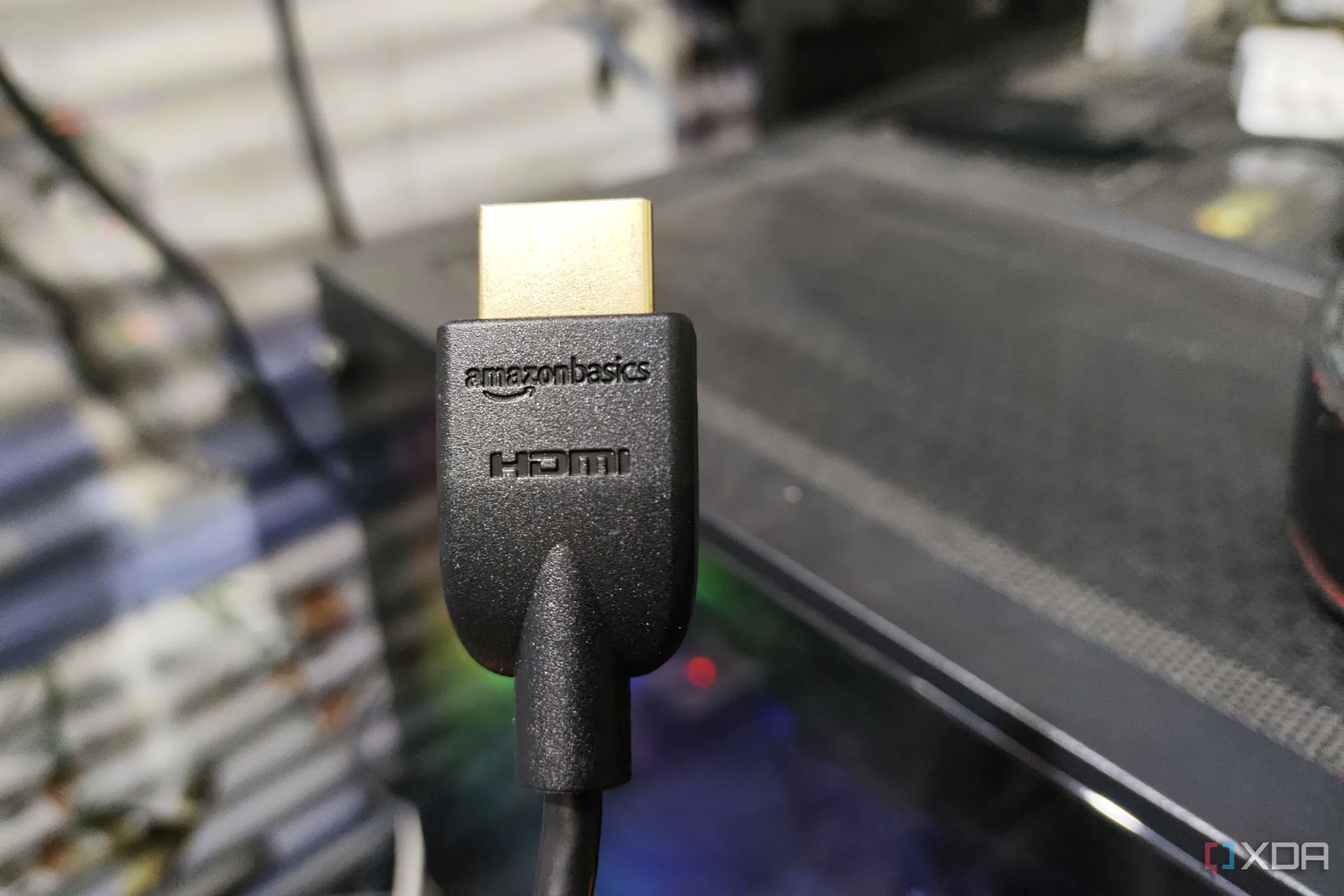 Cáp HDMI 2.1 được cầm trên tay, phía sau là dàn PC, thể hiện giao diện kết nối phổ biến cho nhiều thiết bị điện tử