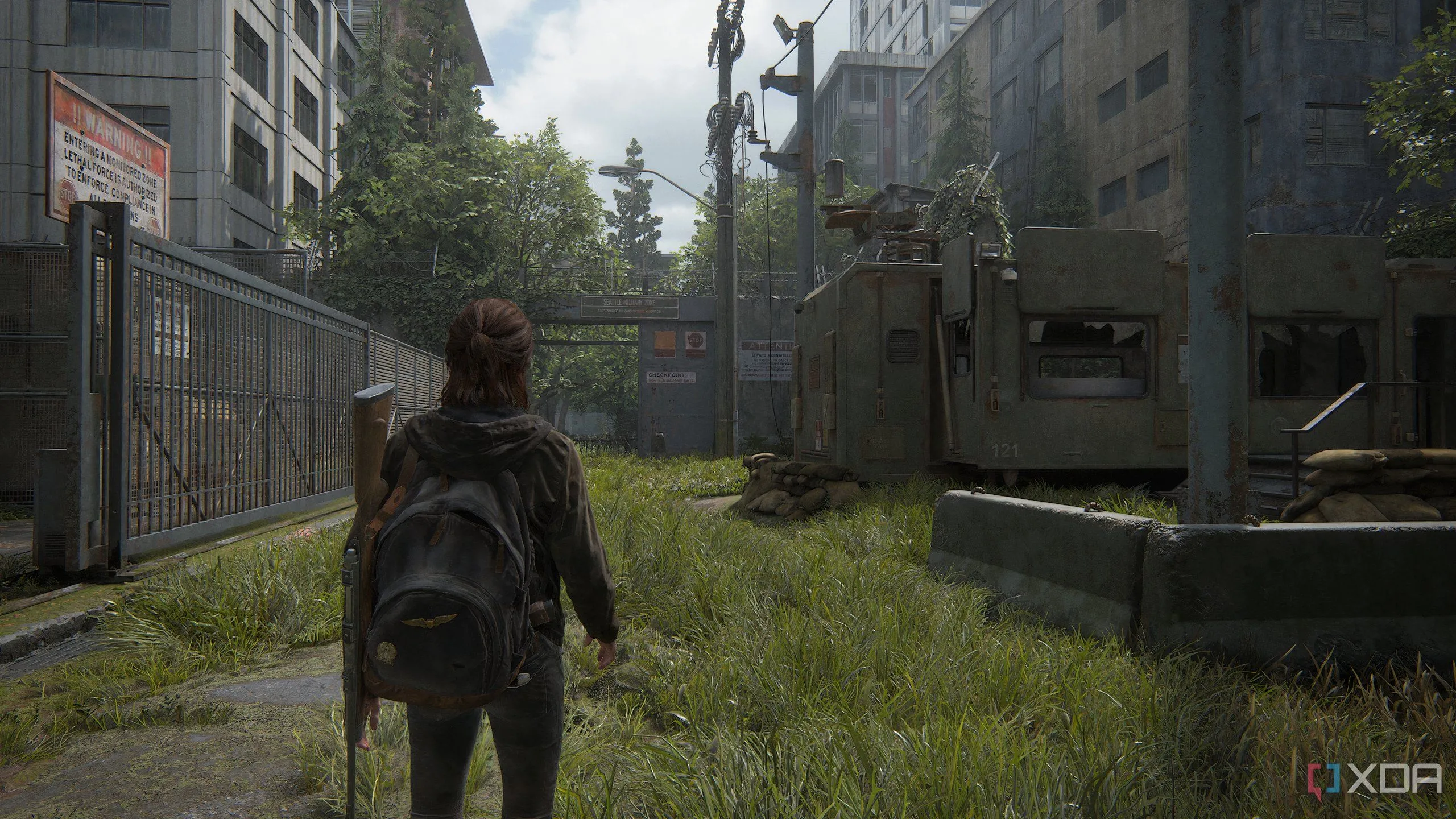 Ellie đi qua khu trại quân sự đổ nát trong The Last of Us Part II Remastered, thể hiện đồ họa môi trường ấn tượng.