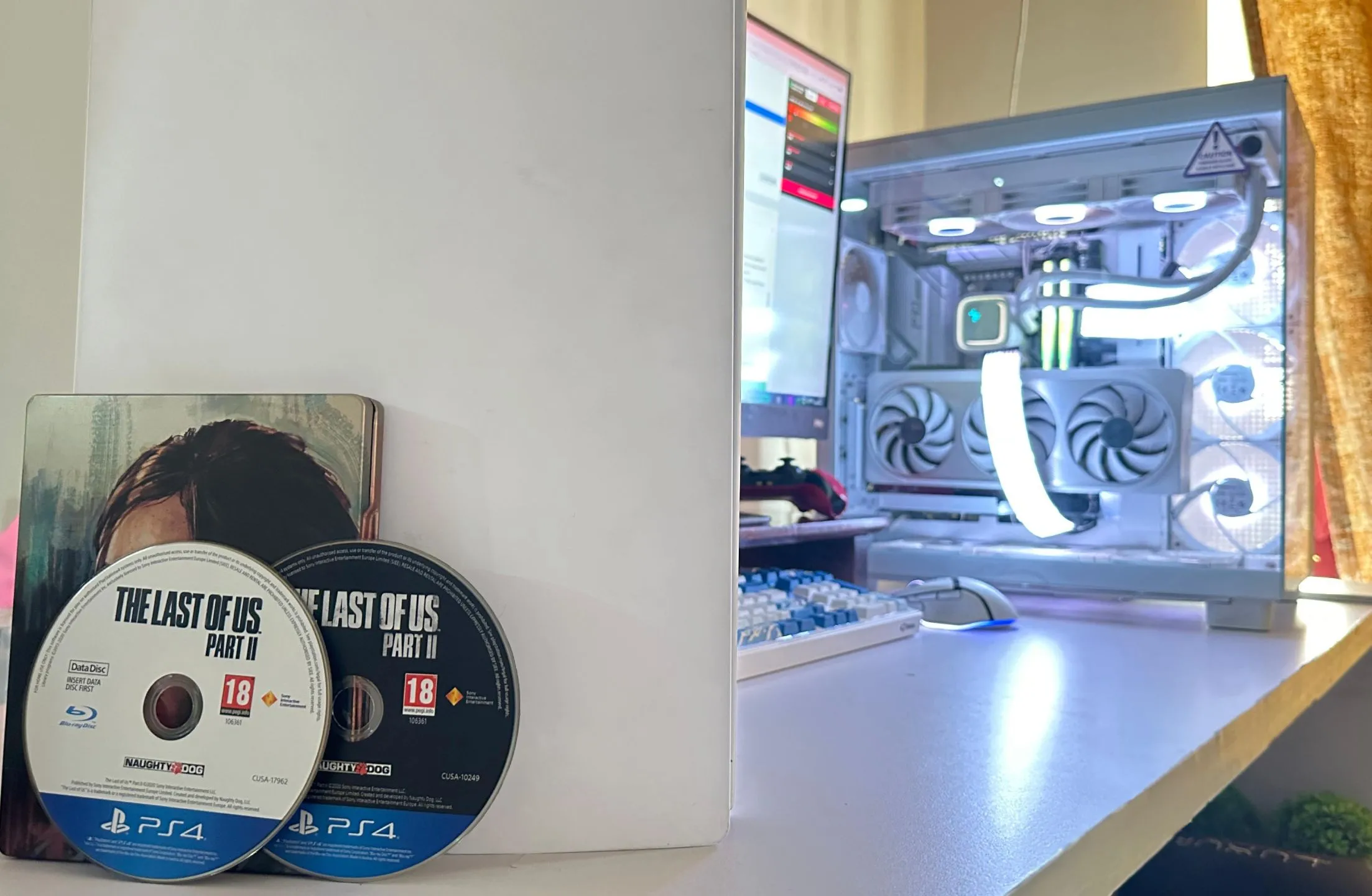 Hai đĩa vật lý của game The Last of Us Part II phiên bản PS4, đặt cạnh PC và PS5, minh họa cho dung lượng game lớn đòi hỏi nhiều đĩa.