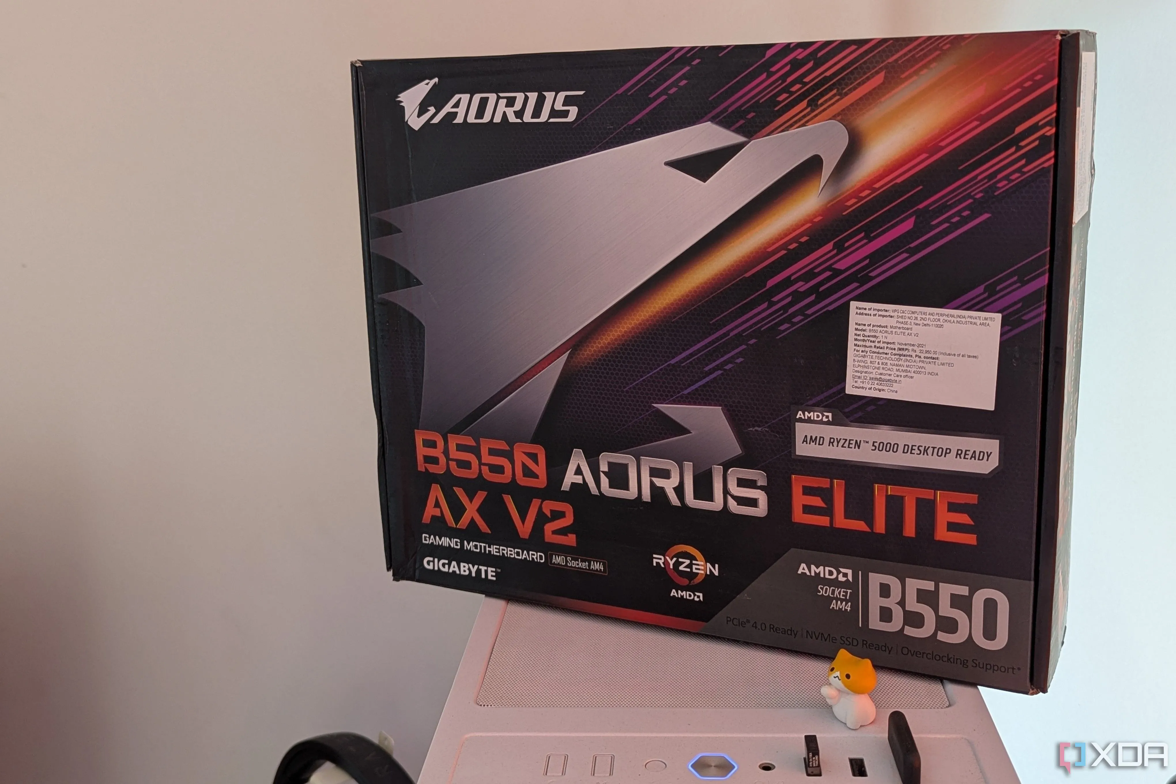 Hộp bo mạch chủ Gigabyte B550 Aorus Elite AX V2 đặt trên vỏ case PC màu trắng, thể hiện sự hấp dẫn của linh kiện mới và thiết kế PC