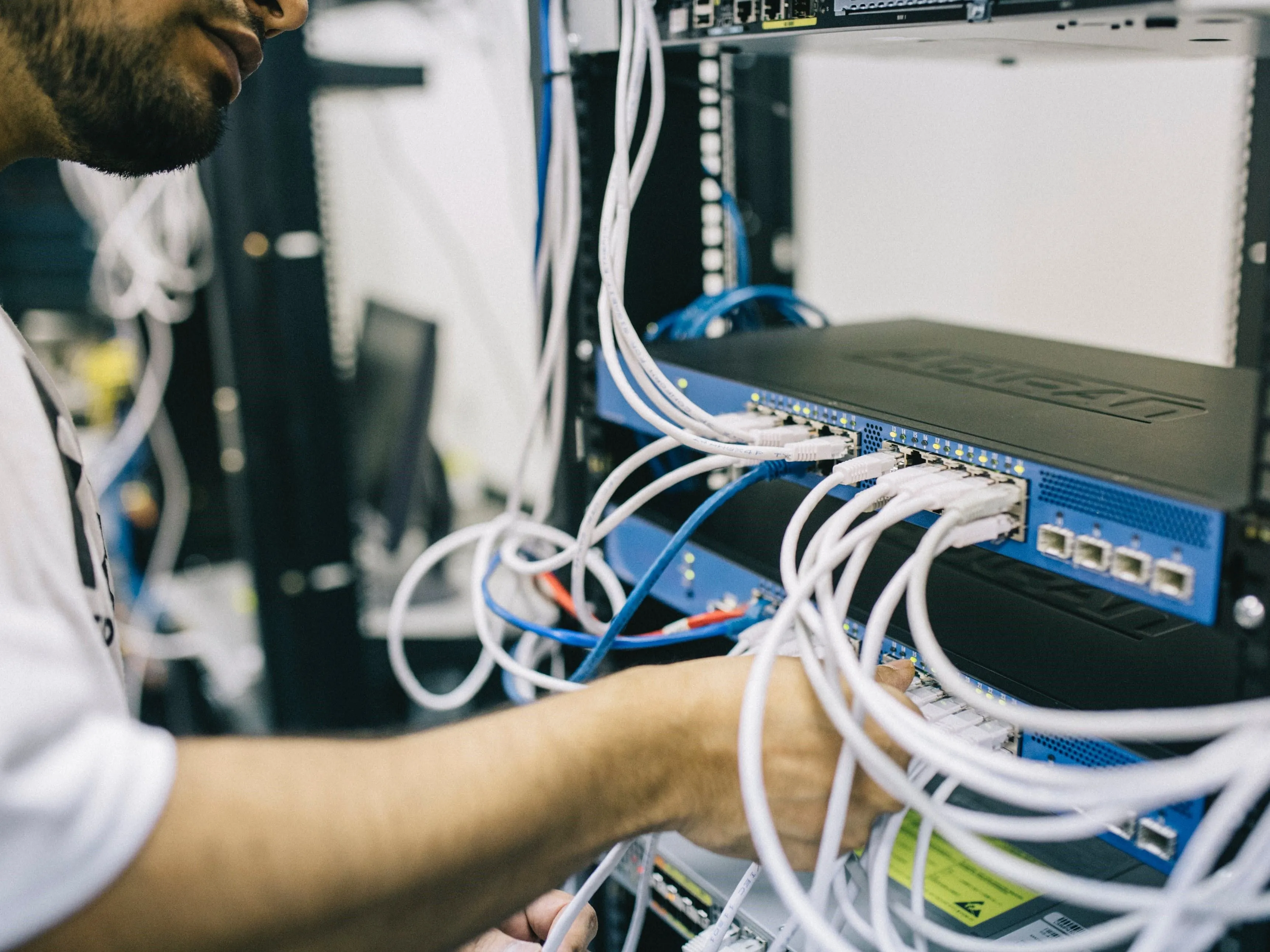 Kỹ sư mạng đang cắm cáp Ethernet vào thiết bị chuyển mạch, nhấn mạnh tầm quan trọng của quản lý và cập nhật bảo mật hệ thống mạng