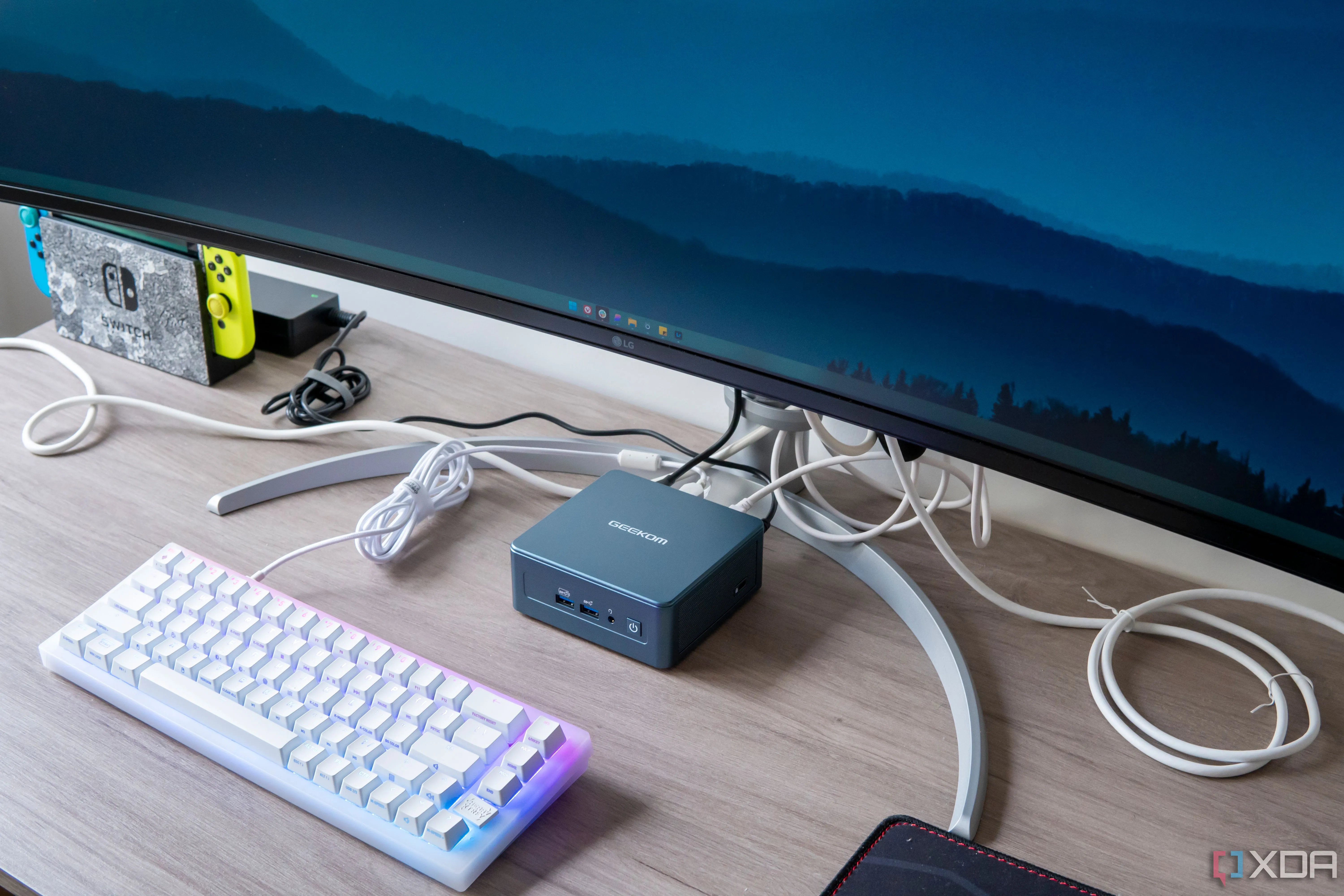 Máy tính mini Geekom Mini IT13 được đặt dưới màn hình với bàn phím ở phía trước, góc nhìn nghiêng