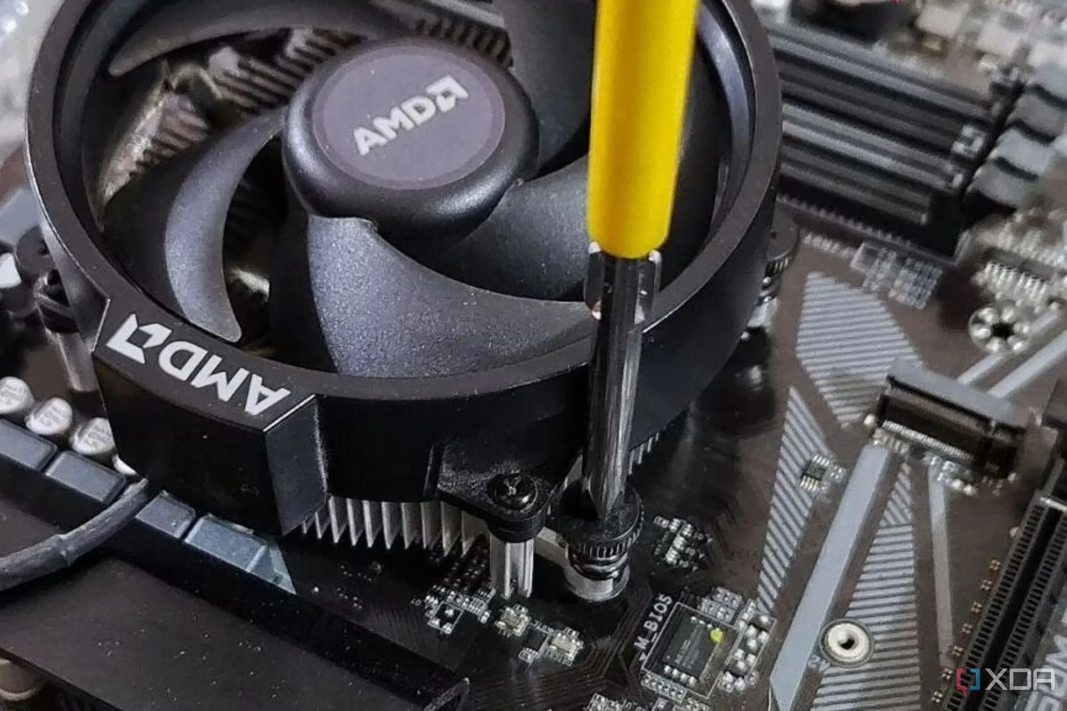 Một chiếc quạt tản nhiệt AMD stock đang được vặn vào bo mạch chủ bằng tua vít Phillips.
