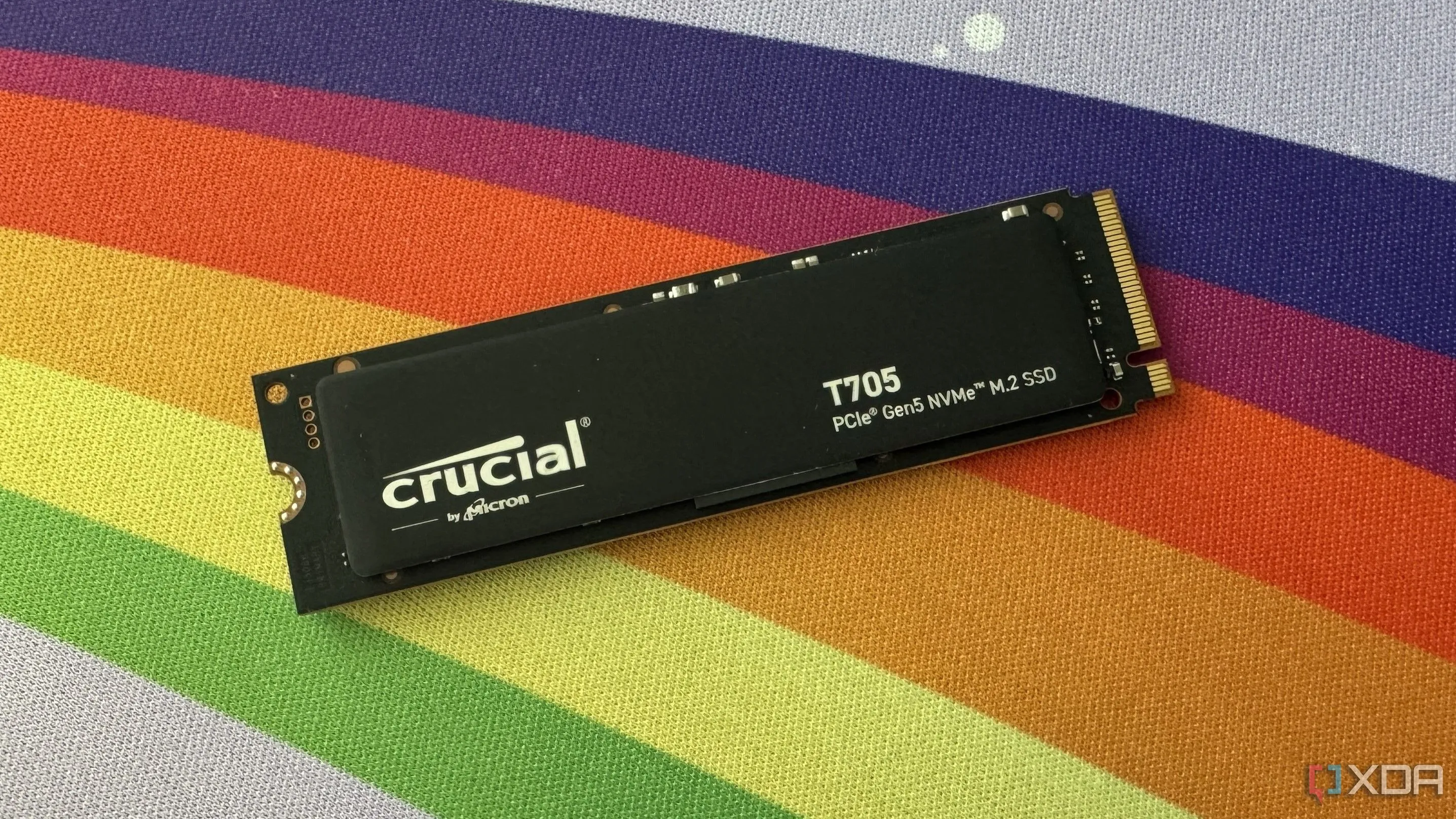 Ổ cứng SSD Crucial T705 đặt trên thảm bàn bàn cầu vồng, minh họa sự đa dạng của các loại SSD trên thị trường với các thông số TBW khác nhau