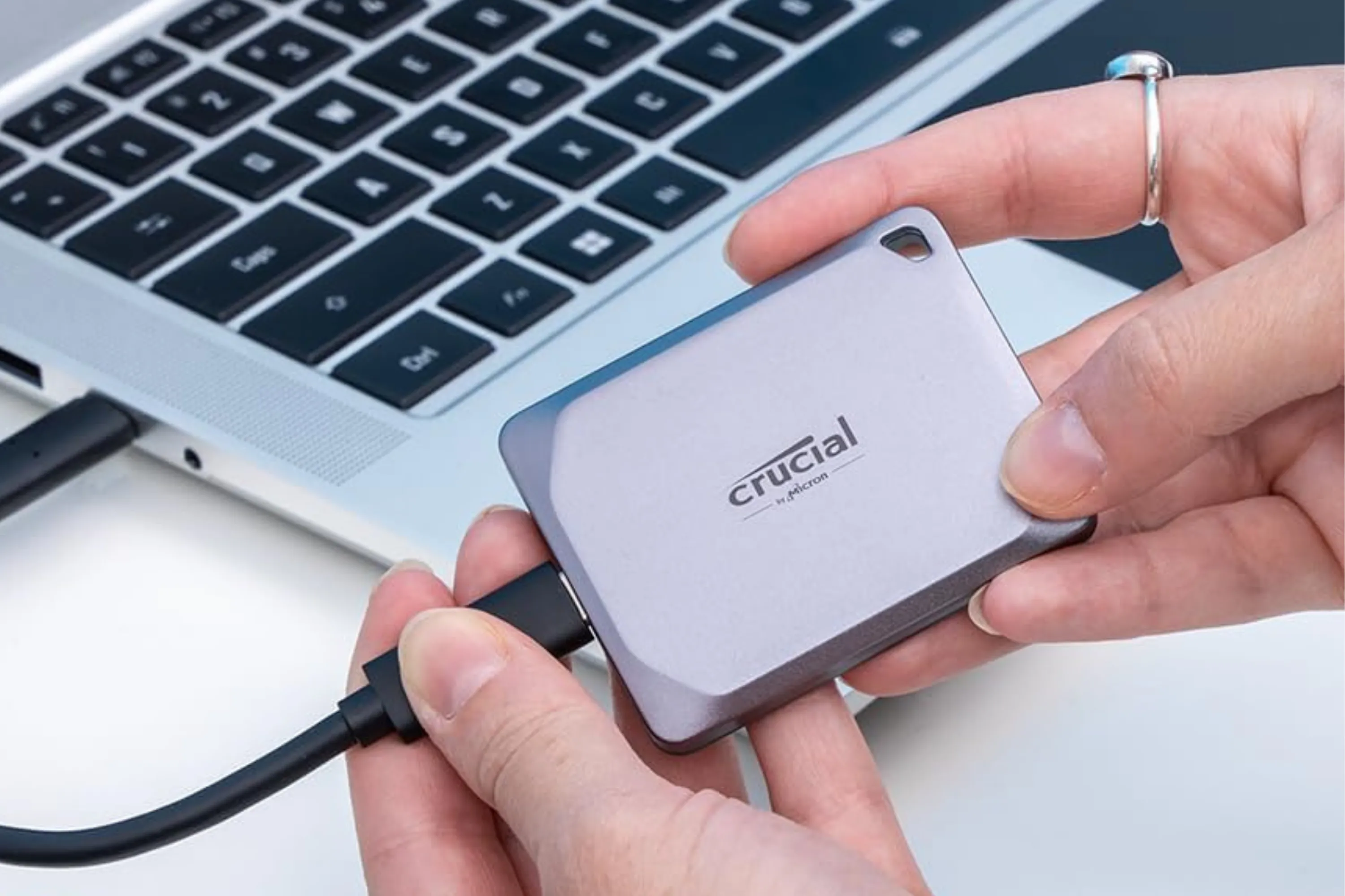 Ổ SSD di động Crucial X9 Pro 1TB đang được cầm trên tay cạnh máy tính