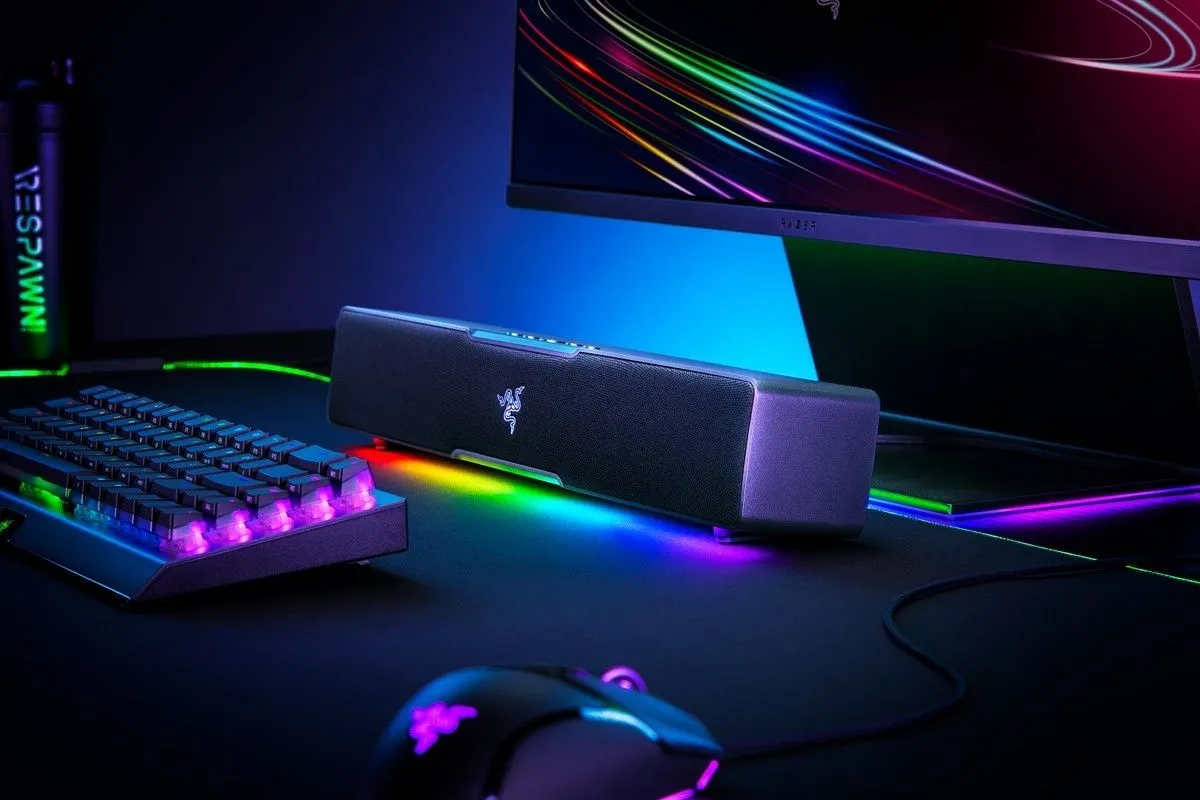 Soundbar Razer Leviathan V2 X với đèn RGB phát sáng, đặt cạnh bàn phím cơ, chuột gaming và màn hình, thể hiện sự tích hợp hoàn hảo vào setup PC.