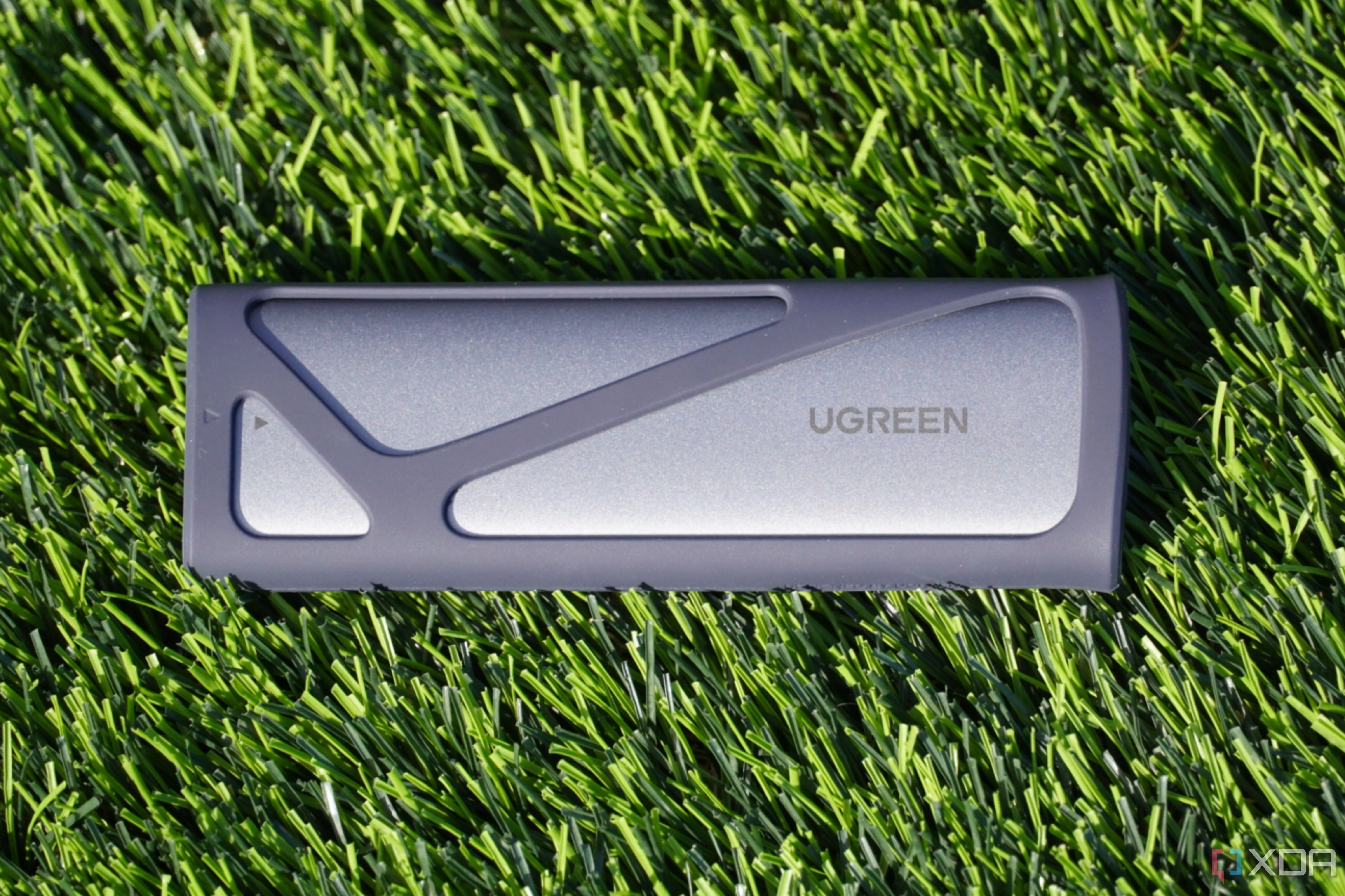 Vỏ bọc SSD Ugreen M.2 NVMe SATA trên nền cỏ, thể hiện thiết bị nhỏ gọn, dễ dàng mang theo